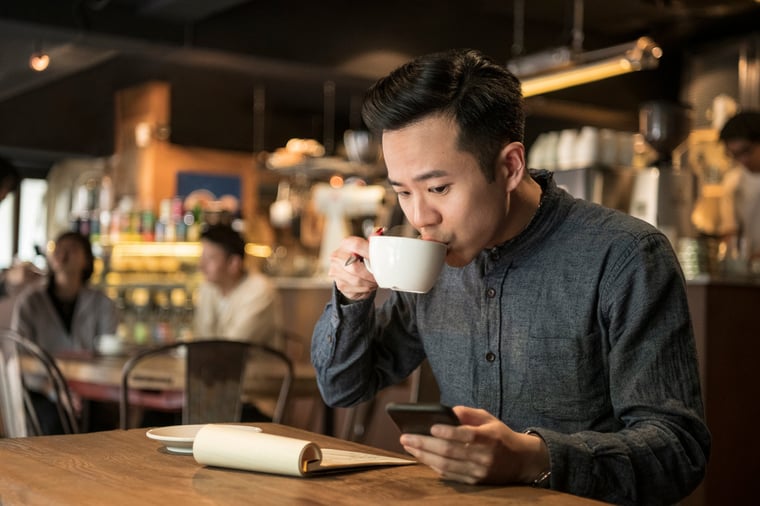 A young businessman writes papers in a cafe and checks her phones.